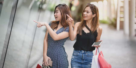 Two beautiful asian women spending their free time shopping at the mall while holding shopping bagの写真素材