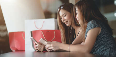 Two beautiful asian women checking their smartphone after spending time shopping in the mallの写真素材