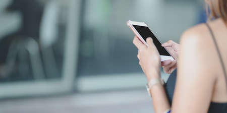 Close-up view of young woman holding smartphone outside the shopping mallの写真素材