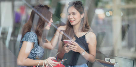 Two beautiful asian women talking together while spending their time shopping at the mall