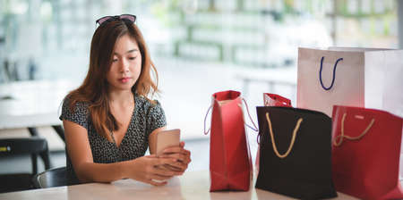 Young asian women checking their smartphone after spending time shopping in the mallの写真素材