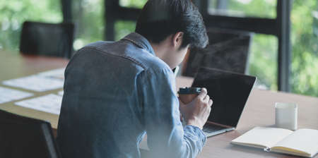 Hard-working male UI web designer working on his new smartphone templates project while using laptop computerの写真素材