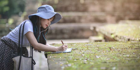Young asian girl taking notes of the old temple while visiting the ancient historical places during the holidayの写真素材