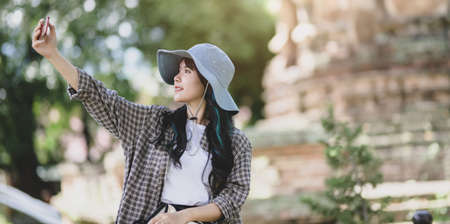 Beautiful asian traveler taking the photo of the old temple with smartphone while visiting the ancient historical placesの写真素材