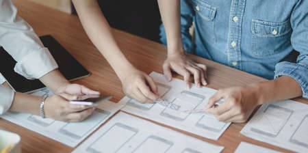 Close-up view of young professional UI graphic designer team discussing on their smartphones templates togetherの写真素材