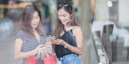 Asian women spending their free time shopping at the mall and chatting together while holding shopping bagの写真素材