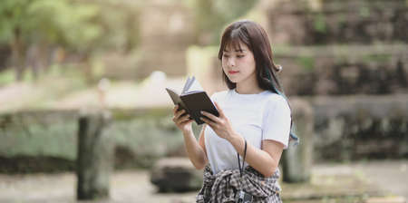 Young female traveler reading the travel guide book while traveling in ancient historical placesの写真素材