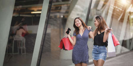 Two beautiful asian women talking together while spending their time shopping at the mallの写真素材