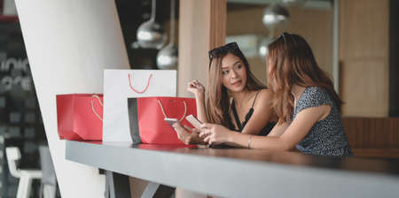 Two beautiful asian women checking their smartphone and chatting together after shopping in the mallの写真素材