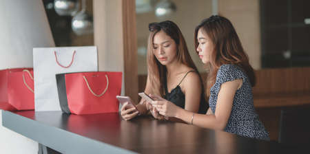 Two beautiful asian women checking their smartphone and chatting together after shopping in the mallの写真素材