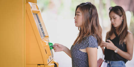 Two young asian female withdrawing the money from a bank card using ATM machine at the mallの写真素材