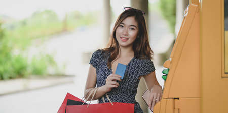 Portrait of beautiful asian woman holding credit card after withdrawing the cash from ATM machineの写真素材
