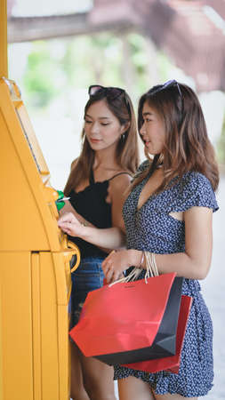 Two young asian female withdrawing the money from a bank card using ATM machine at the mallの写真素材