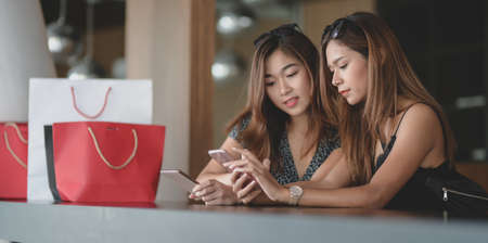 Two beautiful asian women checking their smartphone and chatting together after shopping in the mallの写真素材