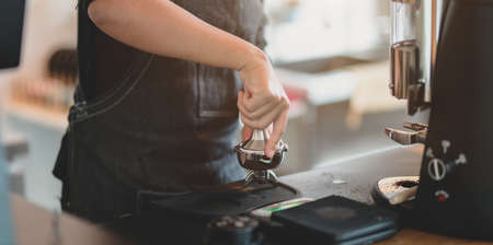 Close-up view of female barista hand's grinding coffee with grinder machine in coffee shopの写真素材