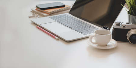 Comfortable photographer workplace with open laptop, coffee cup and office supplies on white wooden deskの写真素材