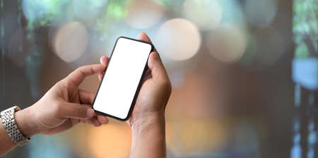 Close-up view of man holding blank screen smartphone with blurry bokeh backgroundの写真素材