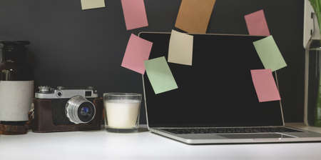 Trendy photographer workplace with open laptop, vintage camera and colourful sticky notes with black wall backgroundの写真素材