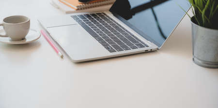 Cozy photographer workplace with open laptop, coffee cup and office supplies on white wooden desk with copy spaceの写真素材