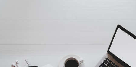 Top view of minimal workplace with laptop computer, coffee cup and office supplies on white wooden desk with copy spaceの写真素材