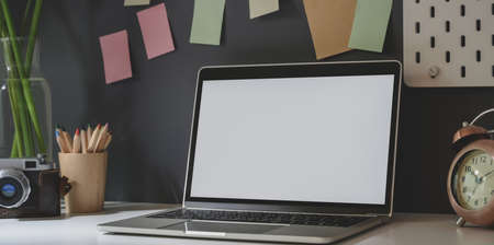 Open blank screen laptop with office supplies in dark trendy photographer workplace with colourful sticky notesの写真素材