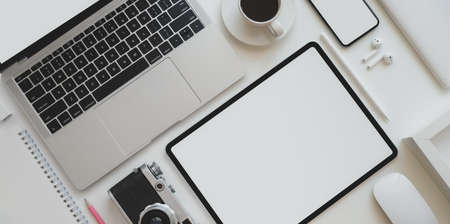 Top view of photographer workplace with blank screen tablet, laptop computer, vintage camera and office supplies on white table backgroundの写真素材