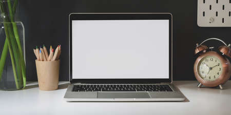 Open blank screen laptop with office supplies in dark trendy workplace on white tableの写真素材