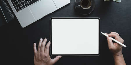 Overhead shot of man writing on blank screen tablet on black leather background with office suppliesの写真素材