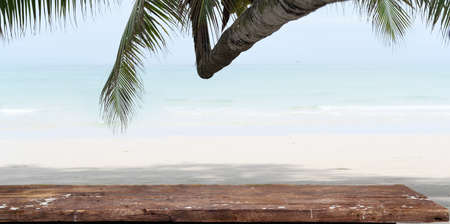 Empty rustic desk with copy space and coconut tree with beautiful tropical beach in the backgroundの写真素材