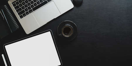 Top view of dark workplace with blank screen tablet and laptop computer on black leather backgroundの写真素材