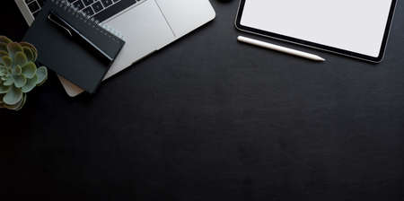 Top view of dark workplace with copy space, blank screen tablet and laptop computer on black leather backgroundの写真素材