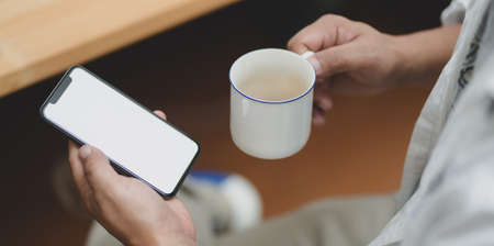 Close-up view of businessman holding blank screen smartphone while drinking a cup of coffeeの写真素材