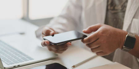 Close-up view of young professional freelancer looking for new concept on smartphone in his modern officeの写真素材