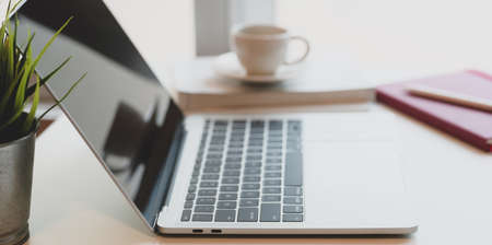 Side view of comfortable workplace with open laptop computer, coffee cup and office suppliesの写真素材