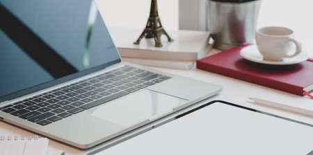 Cropped shot of comfortable workplace with open laptop computer, tablet, coffee cup and office suppliesの写真素材