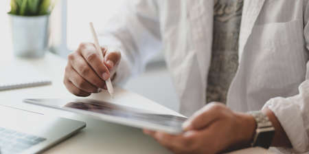 Cropped shot of young freelancer writing his idea concept on tablet for his upcoming project in modern office roomの写真素材