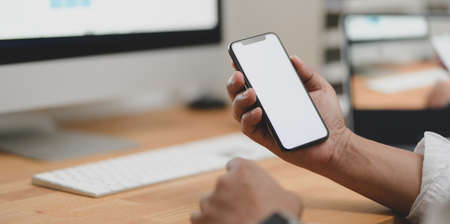 Close-up view of businessman looking for new information on blank screen smartphone in his modern officeの写真素材