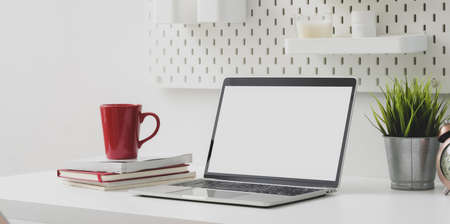 Comfortable workplace with open blank screen laptop computer with red coffee cup and office supplies with decorationsの写真素材
