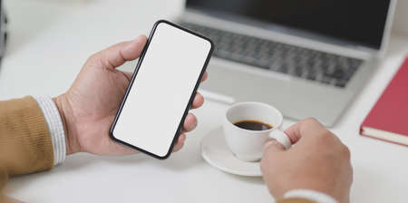 Close-up view of businessman holding blank screen smartphone while drinking a cup of coffee