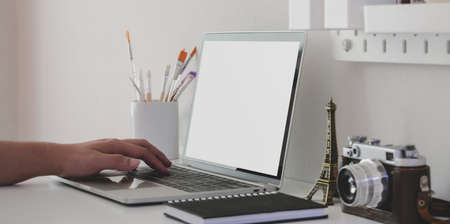 Close-up view of young man typing on blank screen laptop computer in minimal artist workspaceの写真素材