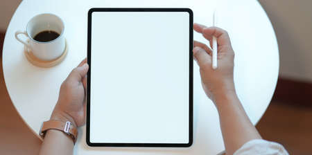 Top view of man holding blank screen tablet with coffee cup in comfortable workspaceの写真素材