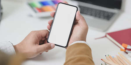 Close-up view of businessman holding blank screen smartphone in minimal workplace full of stationaryの写真素材