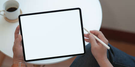 Top view of man holding blank screen tablet with coffee cup in comfortable workspaceの写真素材