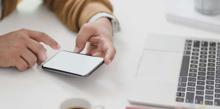 Young businessman looking at information in blank screen smartphone while working on his project with laptop computerの写真素材