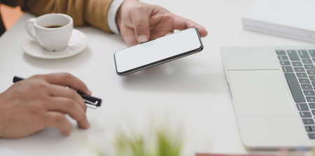 Cropped shot of young businessman working on his project while looking at blank screen smartphone