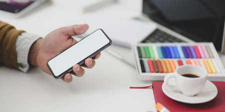 Back to school concepts: Young man holding blank screen smartphone in comfortable workplace with stationeryの写真素材