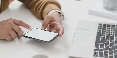 Young businessman looking at information in blank screen smartphone while working on his project with laptop computerの写真素材