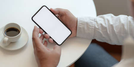 Close-up view of businessman holding blank screen smartphone in comfortable workspaceの写真素材