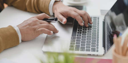 Close-up view of young businessman typing on laptop computer while working on his current projectの写真素材