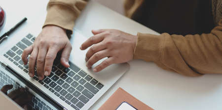 Cropped shot of young man typing on laptop computer while working on his project in comfortable office roomの写真素材